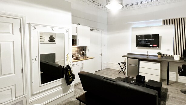 A modern living room with a black sofa, a dining area with a TV, and a kitchen in the background. - Erin Court Mansion -Suite 11 (South Croydon)