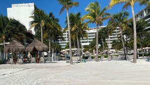 A beach with palm trees, thatched umbrellas, and a sandy area with footprints. - Christmas Heaven in Garza Blanca Mexico (Cancun)