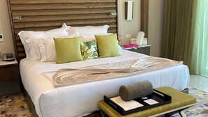 A modern hotel room with a large bed, a bedside table with a lamp, a nightstand, a green curtain, and a patterned rug. - Christmas Heaven in Garza Blanca Mexico (Cancun)