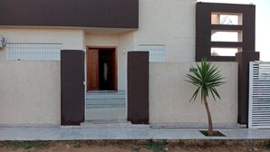 Un bâtiment moderne à la façade plate, avec une porte en bois et un petit palmier au premier plan.
