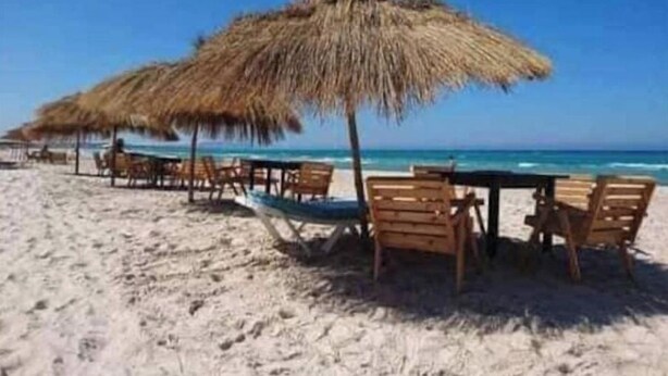 Une plage avec des parasols en chaume et des chaises en bois, ce qui laisse supposer qu’il y a un espace de restauration en bord de mer.