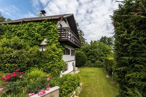 A house with a balcony, surrounded by lush greenery and a well-maintained lawn.