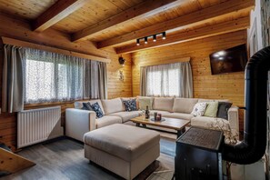 A cozy log cabin interior with a sofa, ottoman, and a fireplace. - Cottage with pool playground and privacy (Vranov)