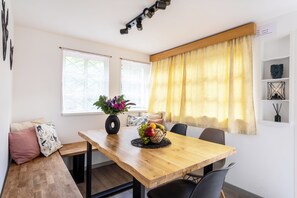 A dining area with a wooden table, chairs, a vase with flowers, and a fruit bowl.