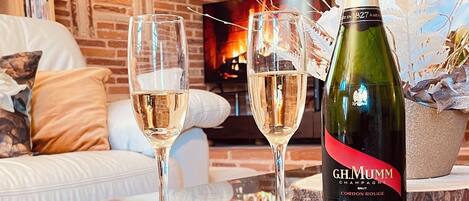 A glass table with two champagne glasses and a bottle of champagne in a living room with a brick wall and a fireplace.
