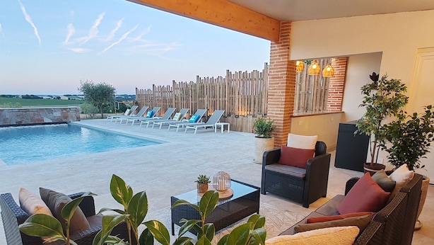 Un espace aménagé au bord de la piscine, avec des chaises longues, un canapé, une table basse et une plante en pot.