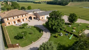 Un grand bâtiment doté d’une cour intérieure, entouré de champs verdoyants et d’arbres.