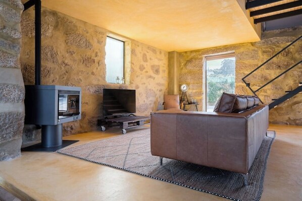 A cozy living room with a stone wall, a fireplace, a sofa, and a staircase.