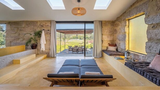 A spacious room with a large bed, a seating area with cushions, a stone wall, and a view of the outdoors. - Lemon Villa-indoor Pool (Porto)
