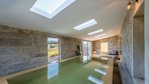 A spacious indoor swimming pool with skylights, stone walls, and a view of the outdoors. - Lemon Villa-indoor Pool (Porto)