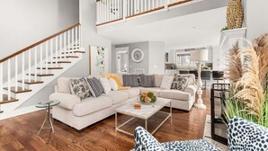 Un vaste salon doté d’un haut plafond, d’un escalier avec des rampes blanches, d’un ensemble de canapés, d’une table basse et d’un coin repas à l’arrière-plan.