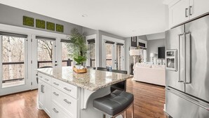 Une cuisine moderne dotée d’un îlot central, de meubles blancs et d’un grand réfrigérateur.