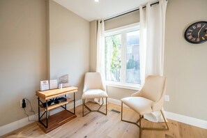 Ein Zimmer mit zwei weißen Stühlen, einem Holztisch und einer Wanduhr.