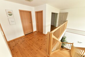 A wooden-floored hallway with two wooden doors, a staircase with wooden railings, and a white wall with framed pictures. - Ferienwohnung Katharinenschule (Eisenach)