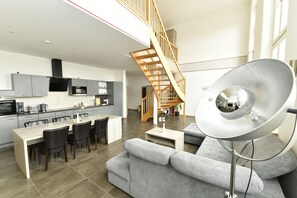 A modern kitchen with grey cabinets, a dining table, and chairs. There is a staircase leading to an upper level. - Ferienwohnung Katharinenschule (Eisenach)