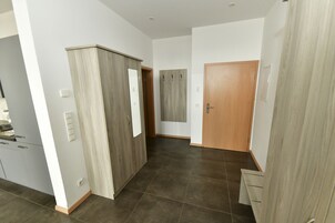 Un interior moderno con zona de cocina, armario de madera y puerta que da a otra habitación.