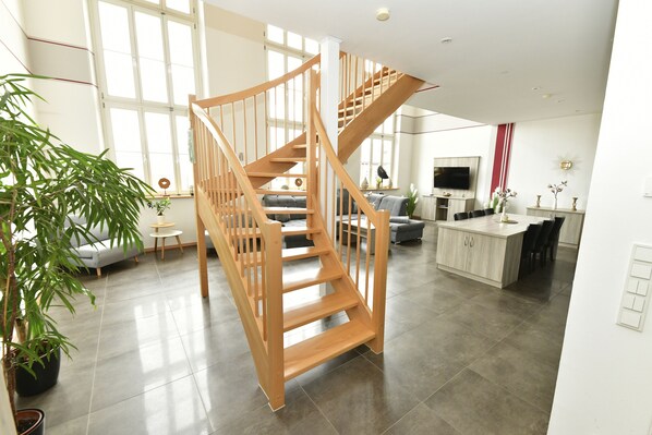A spacious living area with a wooden staircase, a sofa, a dining table, and a TV. - Ferienwohnung Katharinenschule (Eisenach)