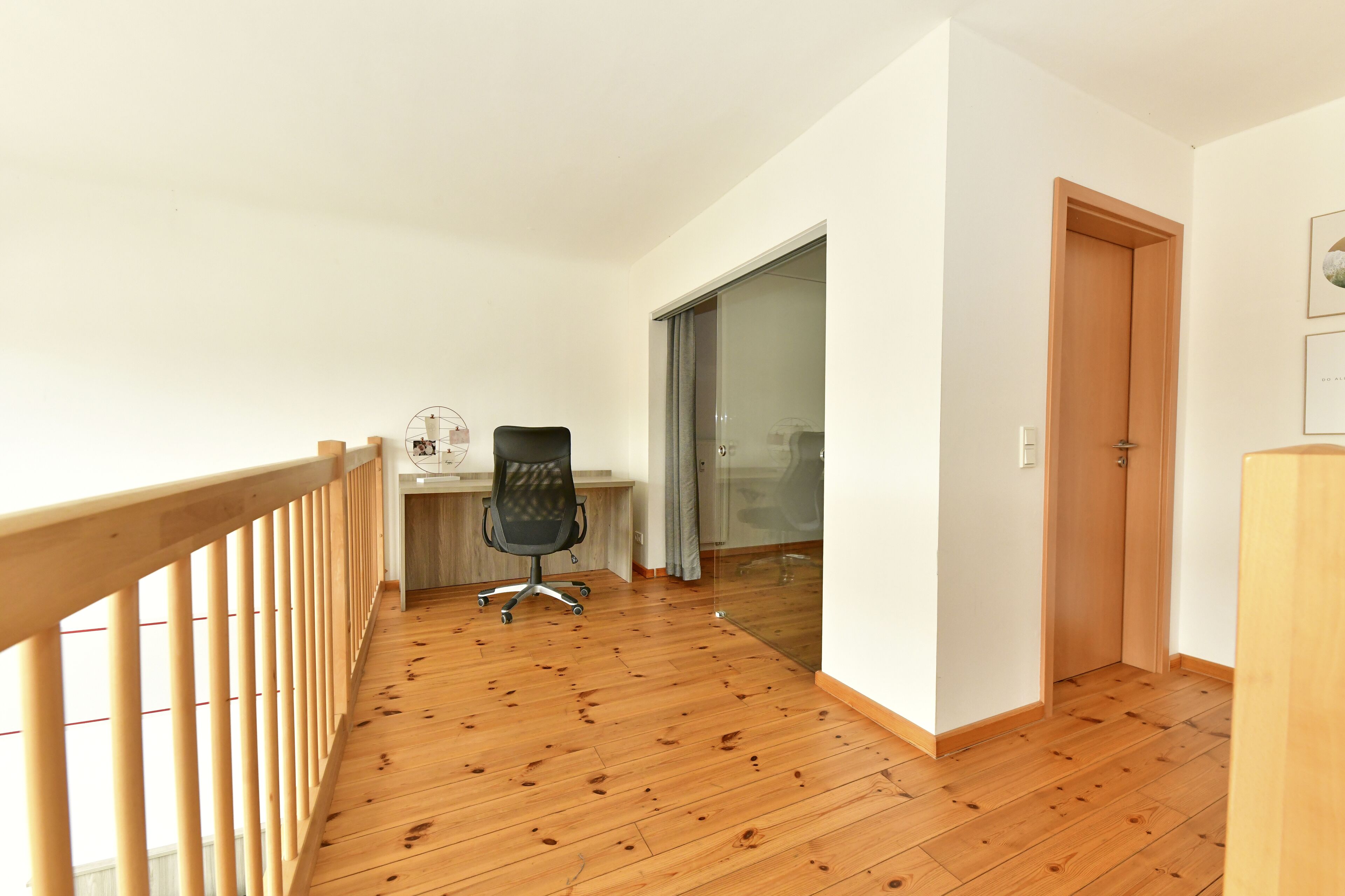Una stanza con pavimento in legno, una scrivania, una sedia e una porta.