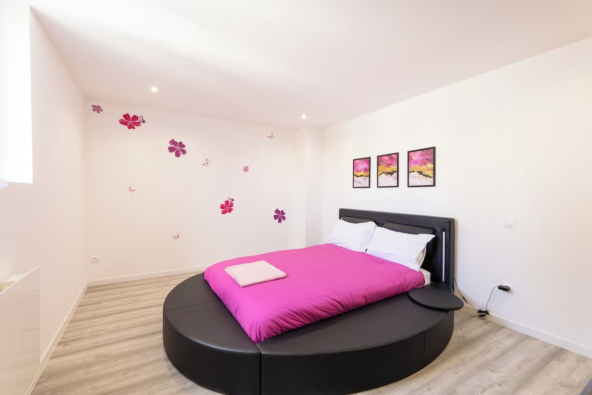 A modern bedroom with a curved bed, white walls, and a wooden floor.