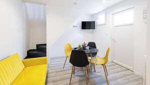 A modern living space with a yellow sofa, a dining table with chairs, and a flat-screen TV mounted on the wall. -  GLM Residences 1 (Saint-Quentin)