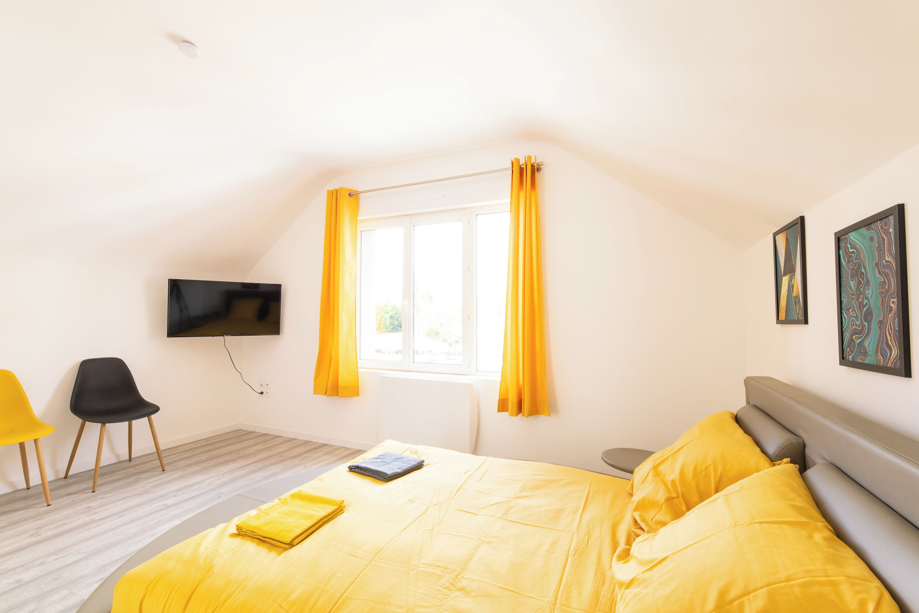 Une chambre à coucher avec un lit, une télévision, une fenêtre avec des rideaux et deux chaises.