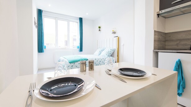 A modern kitchen with a dining area, a bed with a view, and a small kitchenette. -  GLM Residences 1 (Saint-Quentin)