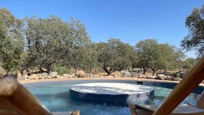A hot tub surrounded by a pool with wooden chairs in the foreground. - Herdade da Saudade - La Casita (São Pedro Gafanhoeira)