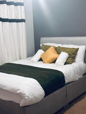 A bed with white bedding, a green throw blanket, and multiple pillows in various colors.