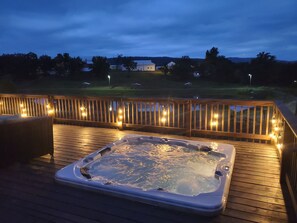 Een hottub op een houten terras, omgeven door sfeerverlichting en een houten balustrade.