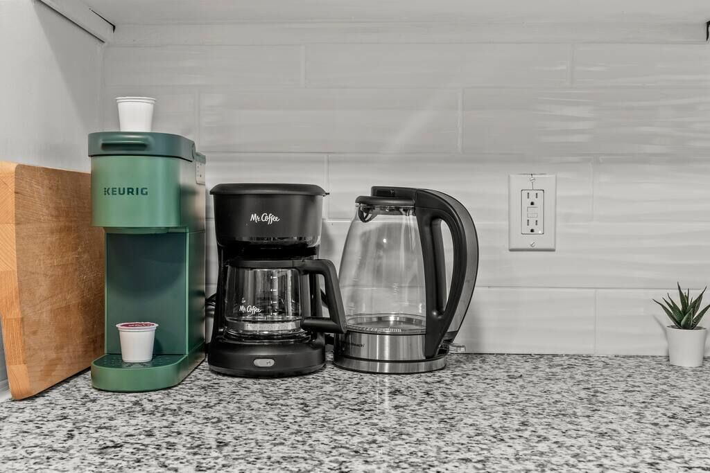 A kitchen with a Keurig coffee maker, a Mr. Coffee coffee maker, and a glass carafe on a granite countertop.