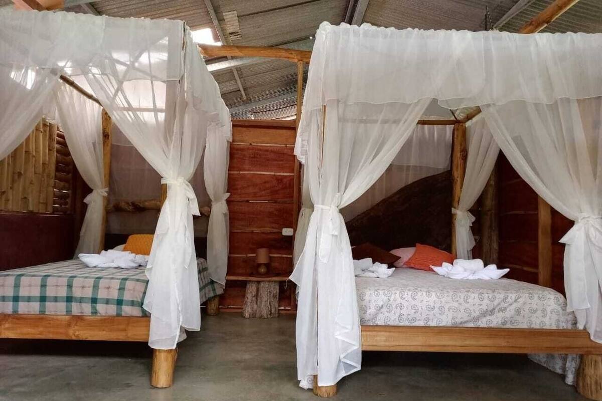 Two wooden beds with white mosquito netting, a checkered bedspread on one, and a patterned bedspread on the other.