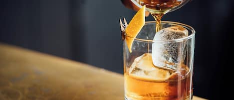 A clear glass with ice cubes and a lemon wedge, with a liquid being poured into it.