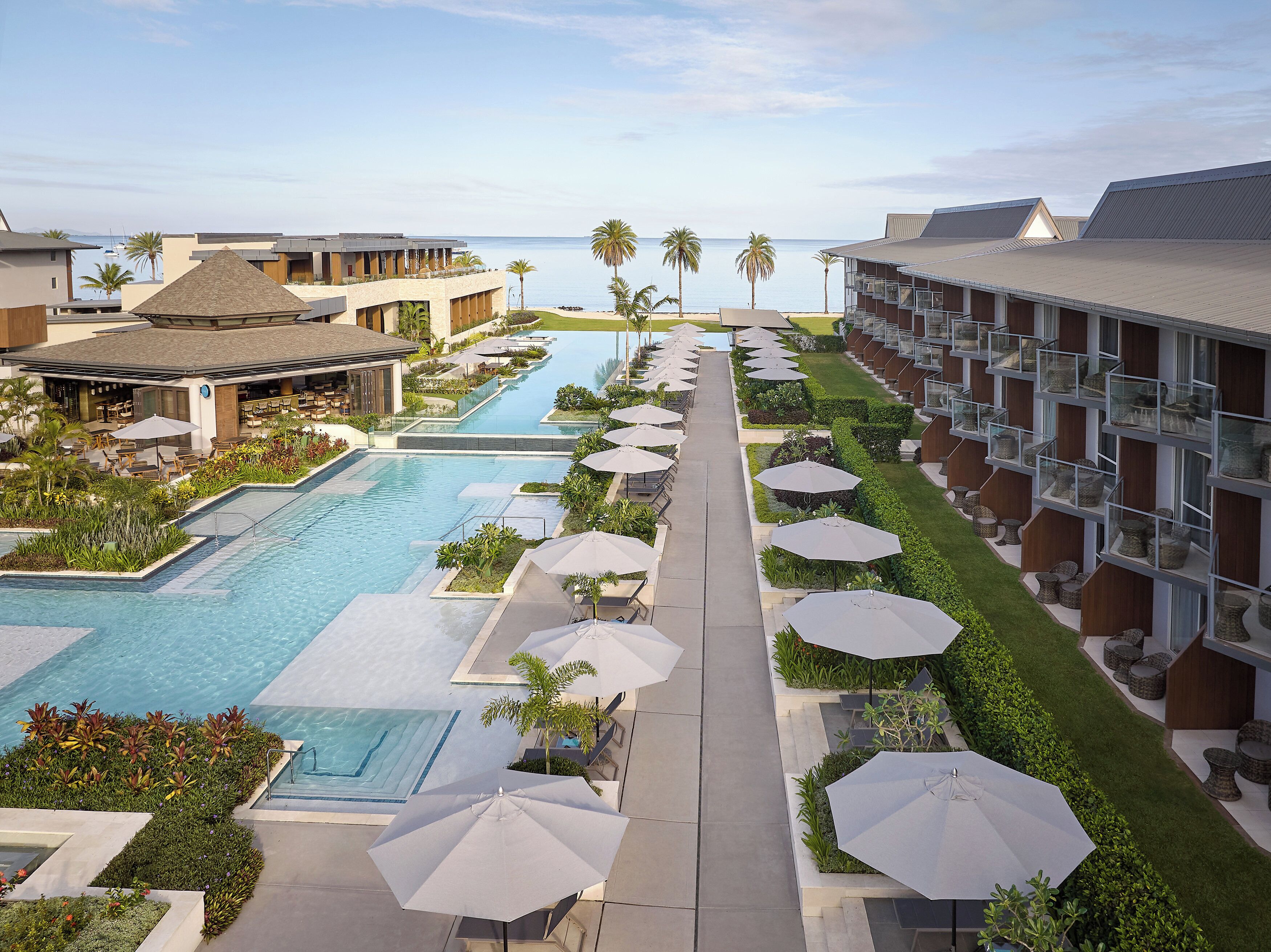 A resort with multiple swimming pools, outdoor seating areas, and a view of the ocean.