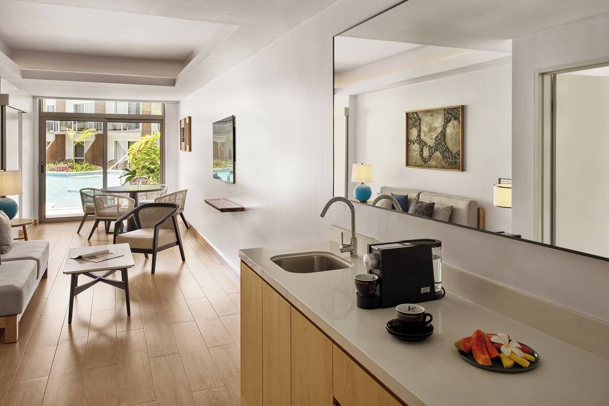 A modern kitchen with a large island, a dining area with chairs, and a view of a pool through the glass door.