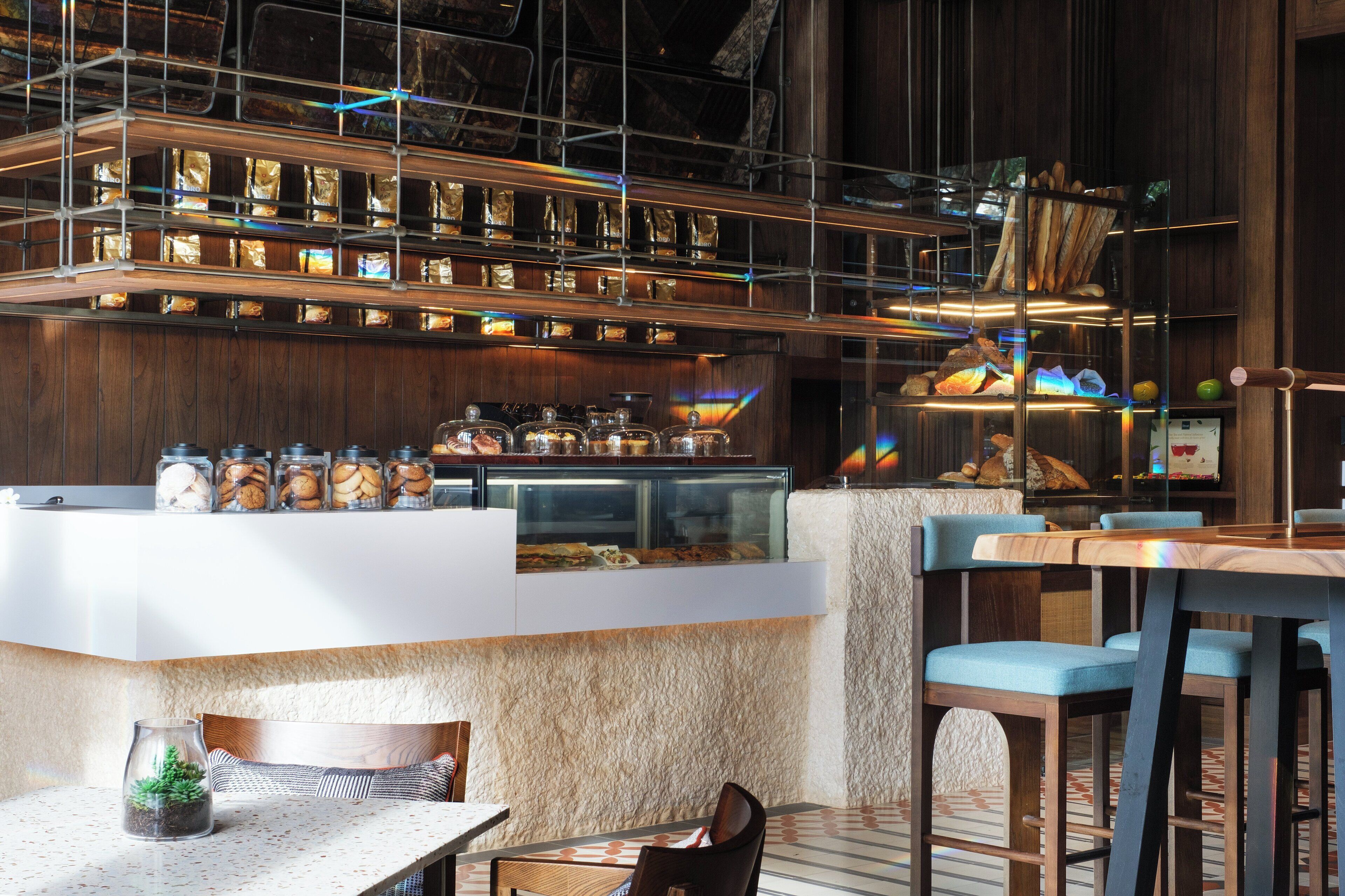 A modern bar area with a counter displaying various food items, a seating area with chairs and tables, and a decorative plant on the table.