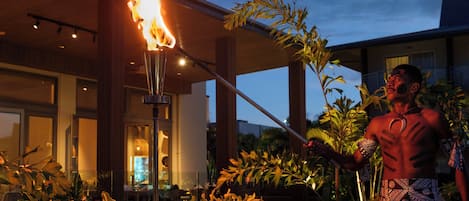 A person performing with a flaming torch in an outdoor setting with a modern building in the background.