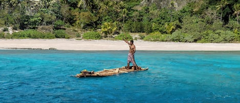 A person standing on a floating platform in clear blue water, surrounded by lush greenery and a sandy beach.