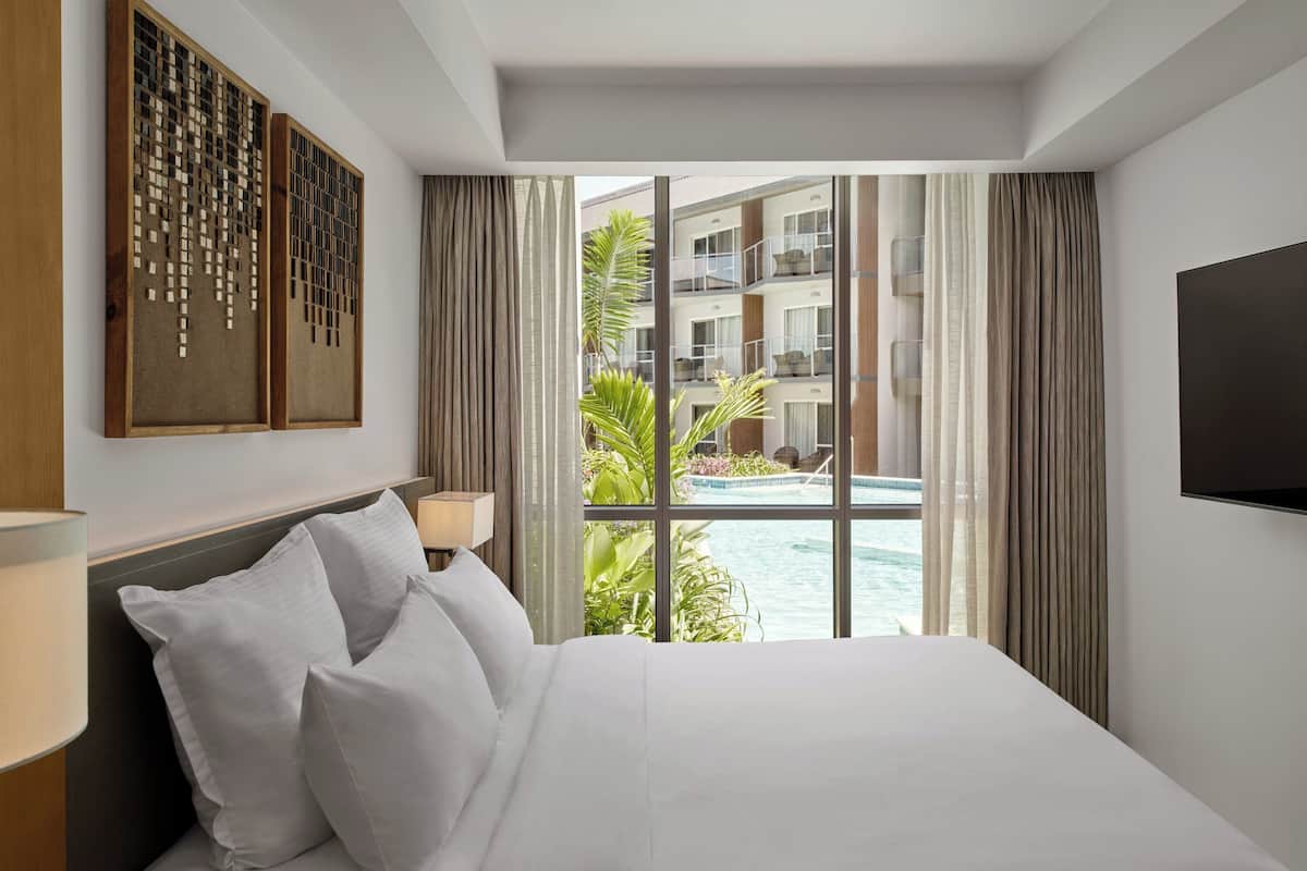 A hotel room with a large bed, a TV mounted on the wall, and a view of a swimming pool and building.