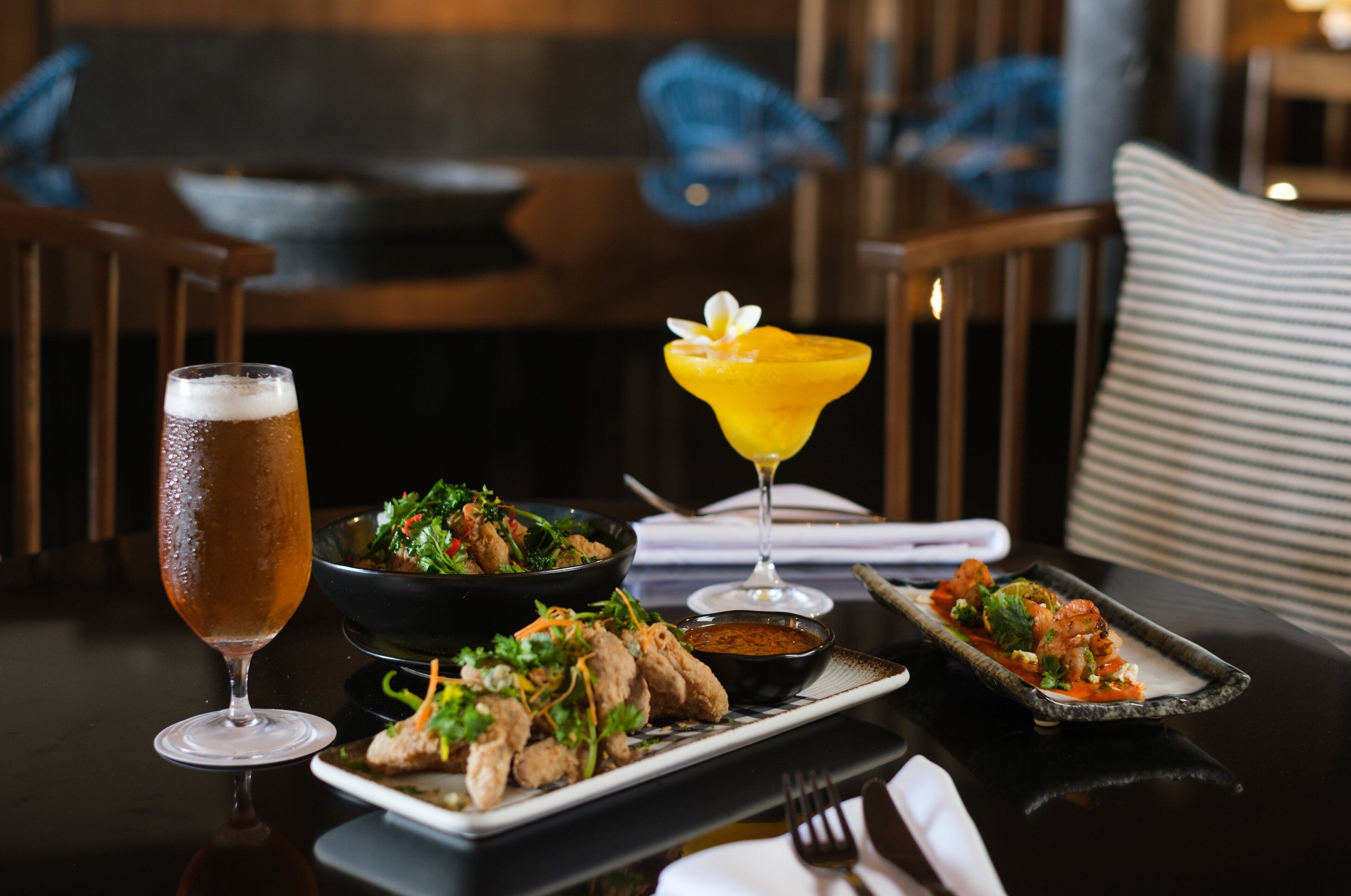 A dining table with a beer glass, a cocktail glass, and plates of food.