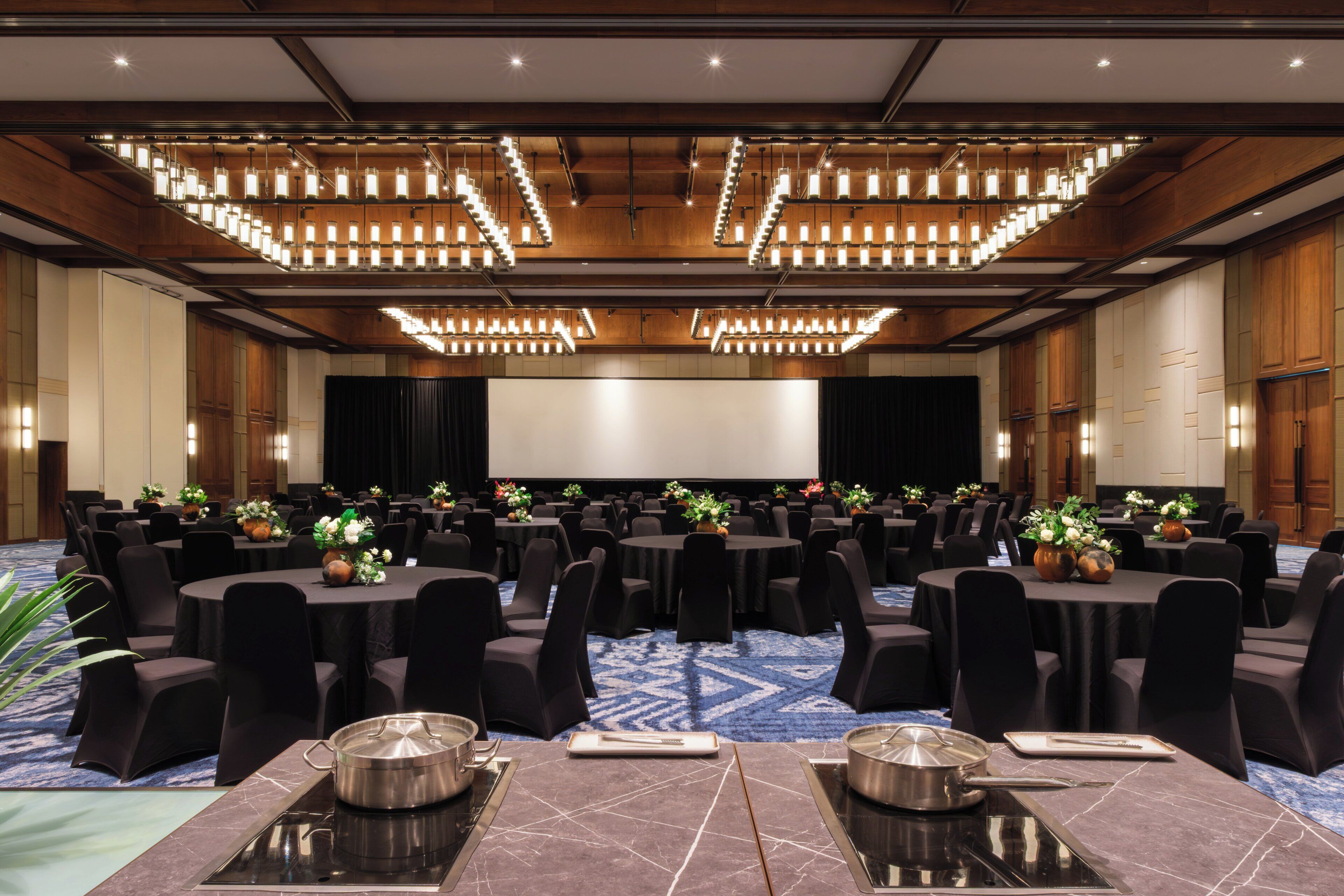 A large conference room with multiple tables, black chairs, and a stage with a screen.