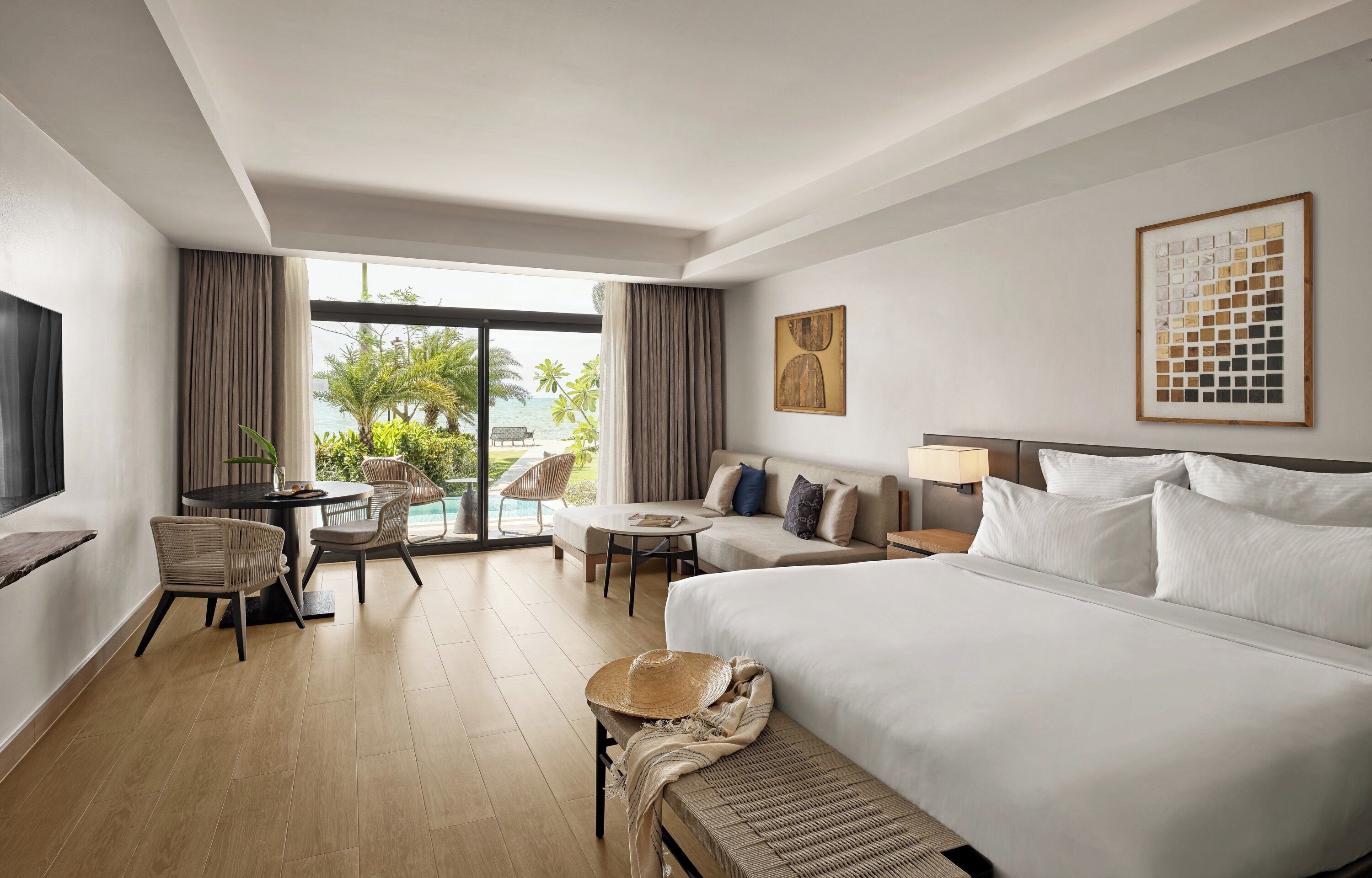 Habitación de hotel con una cama grande, un sofá, una mesa de comedor con sillas y vistas al exterior.