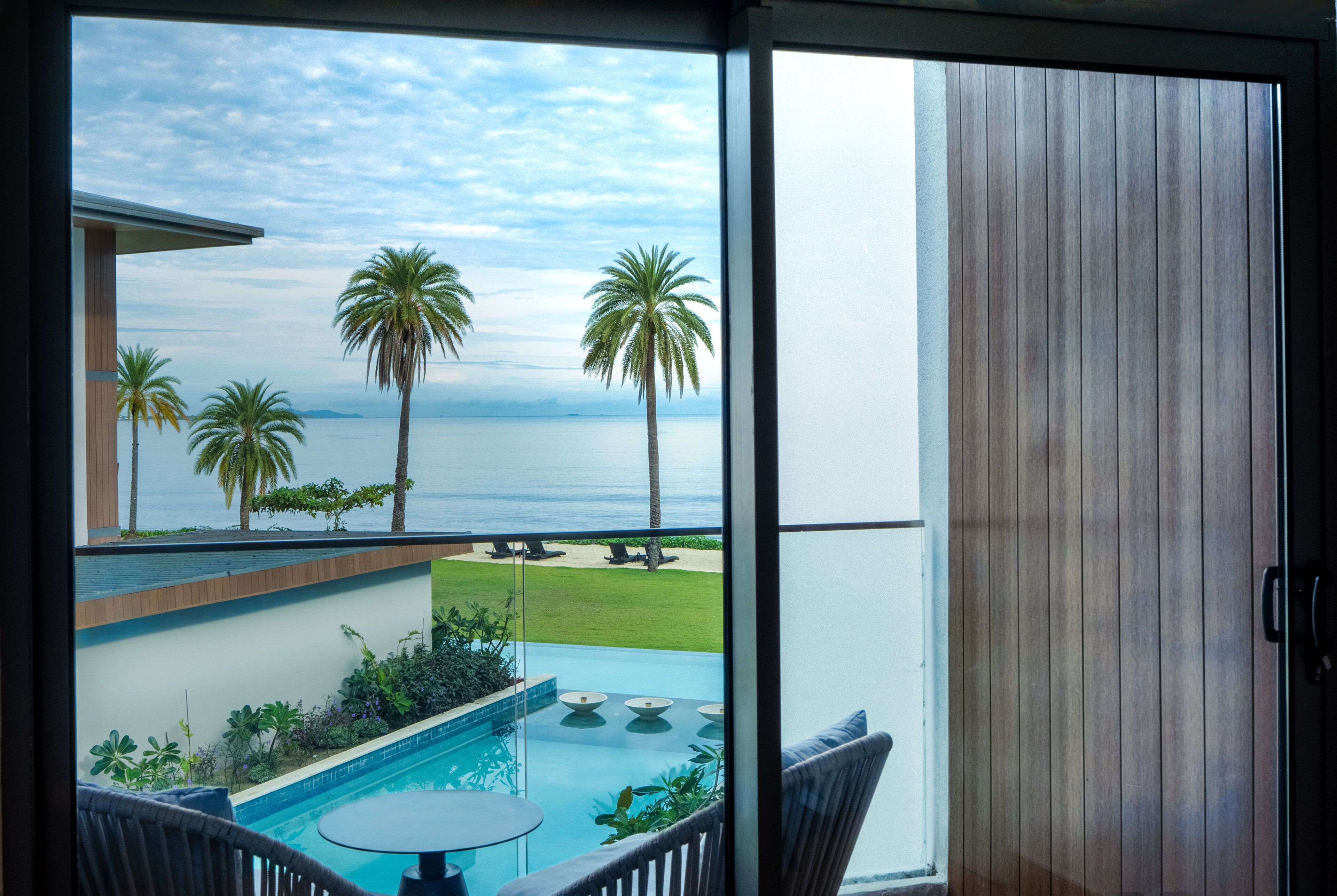 Un balcón con vistas al mar, palmeras y una piscina.