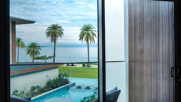 Een balkon met uitzicht op zee, palmbomen en een zwembad.