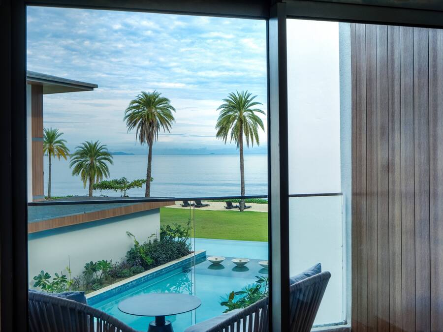Een balkon met uitzicht op zee, palmbomen en een zwembad.