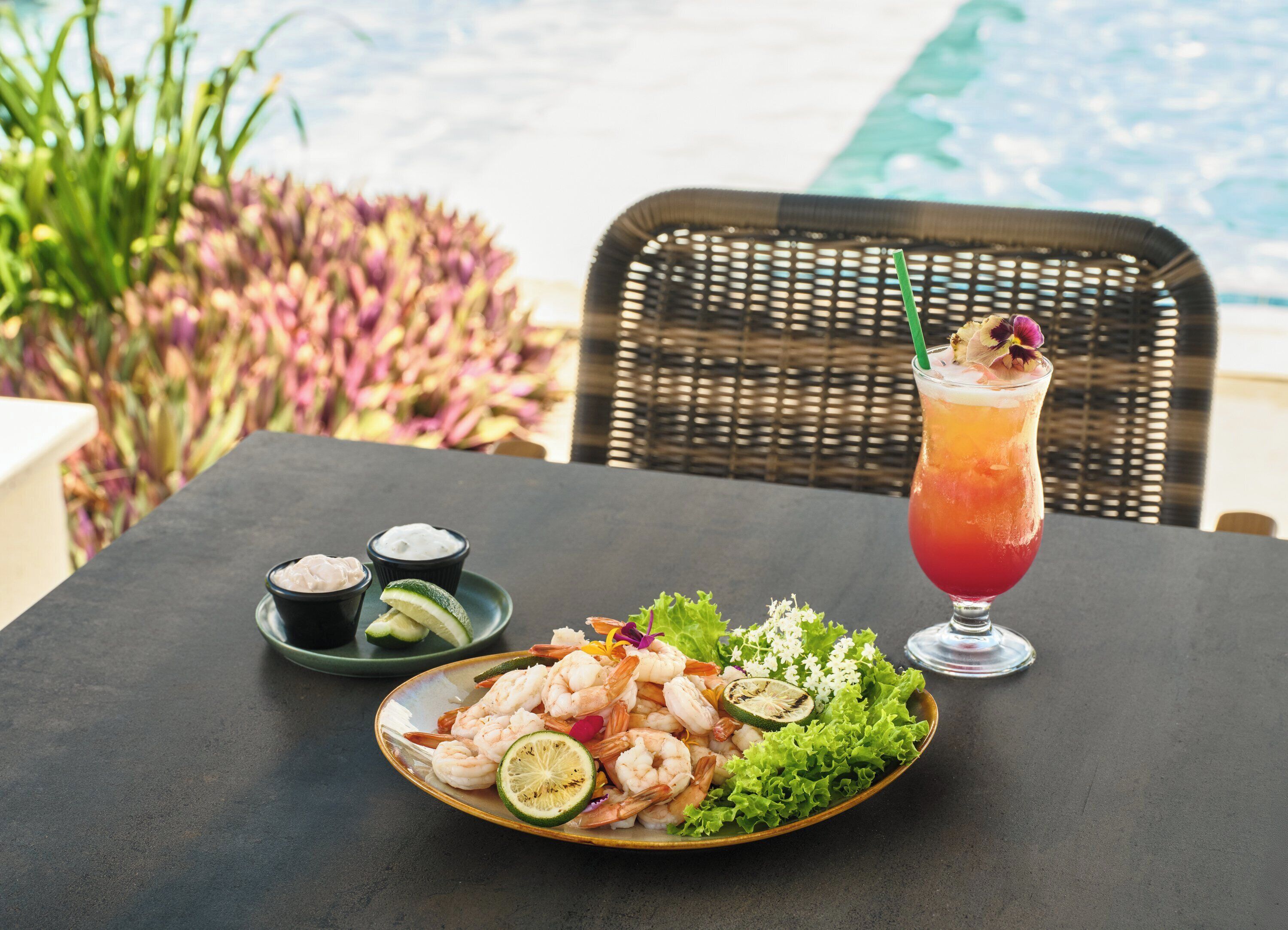 Une table avec une assiette de crevettes, une boisson et de petits ramequins contenant des condiments.
