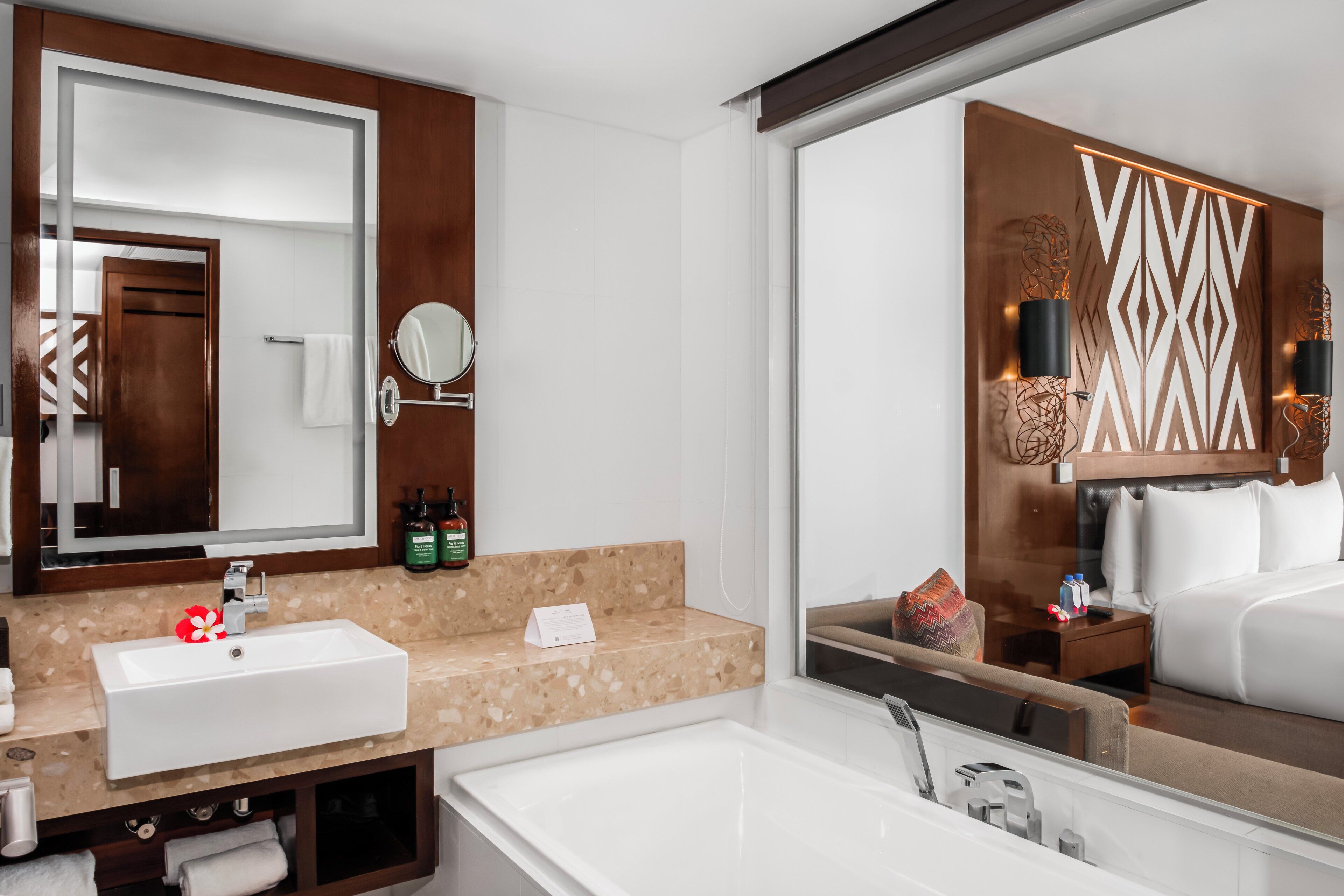 Ein modernes Badezimmer mit einem großen Spiegel, einem Waschbecken, einer Badewanne und einem Waschtisch mit Pflegeprodukten.