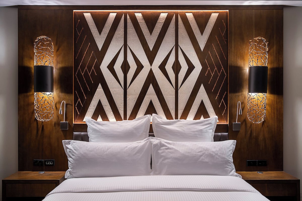 A modern hotel room with a large bed, two bedside tables, and a geometric-patterned headboard.