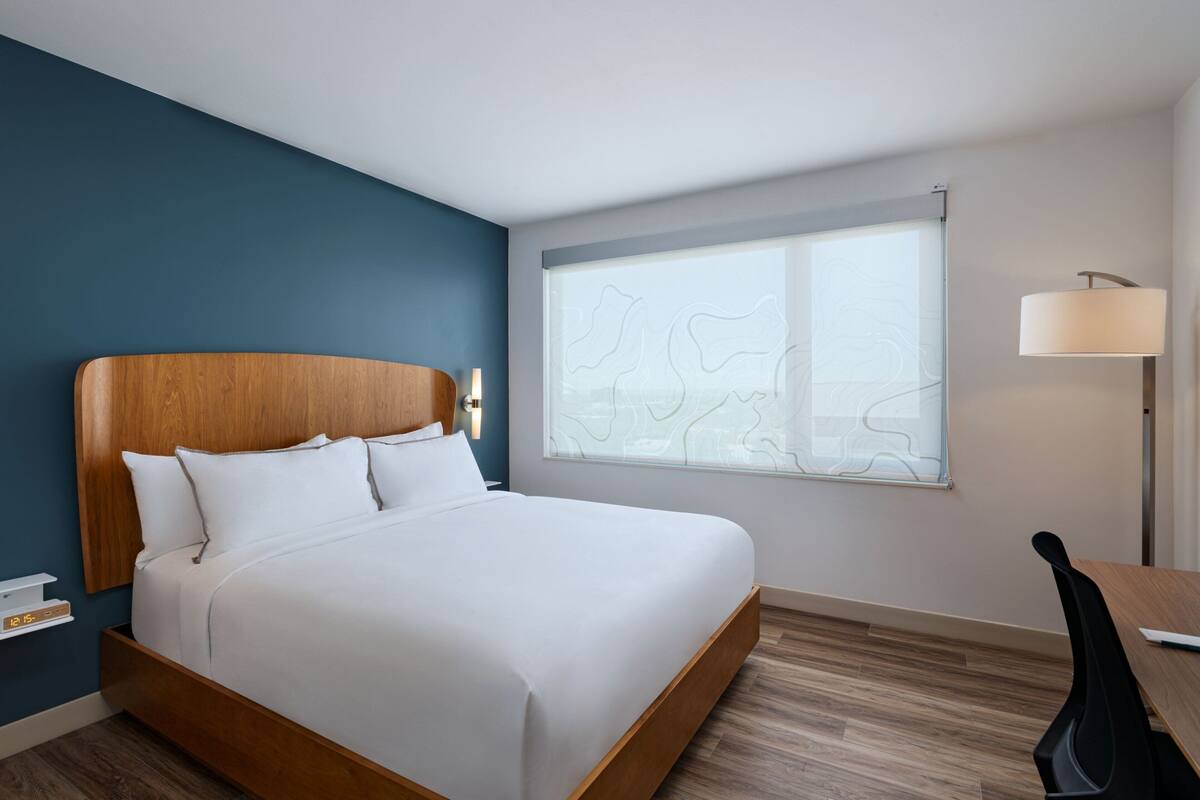 Une chambre d’hôtel moderne avec un lit en bois, un bureau et une grande fenêtre donnant sur un beau paysage.