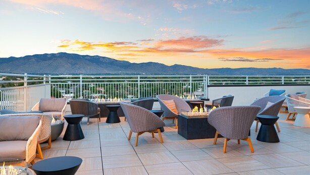 A rooftop terrace with outdoor seating, a fire pit, and a view of mountains during sunset. - Element by Marriott Albuquerque Uptown (Albuquerque)