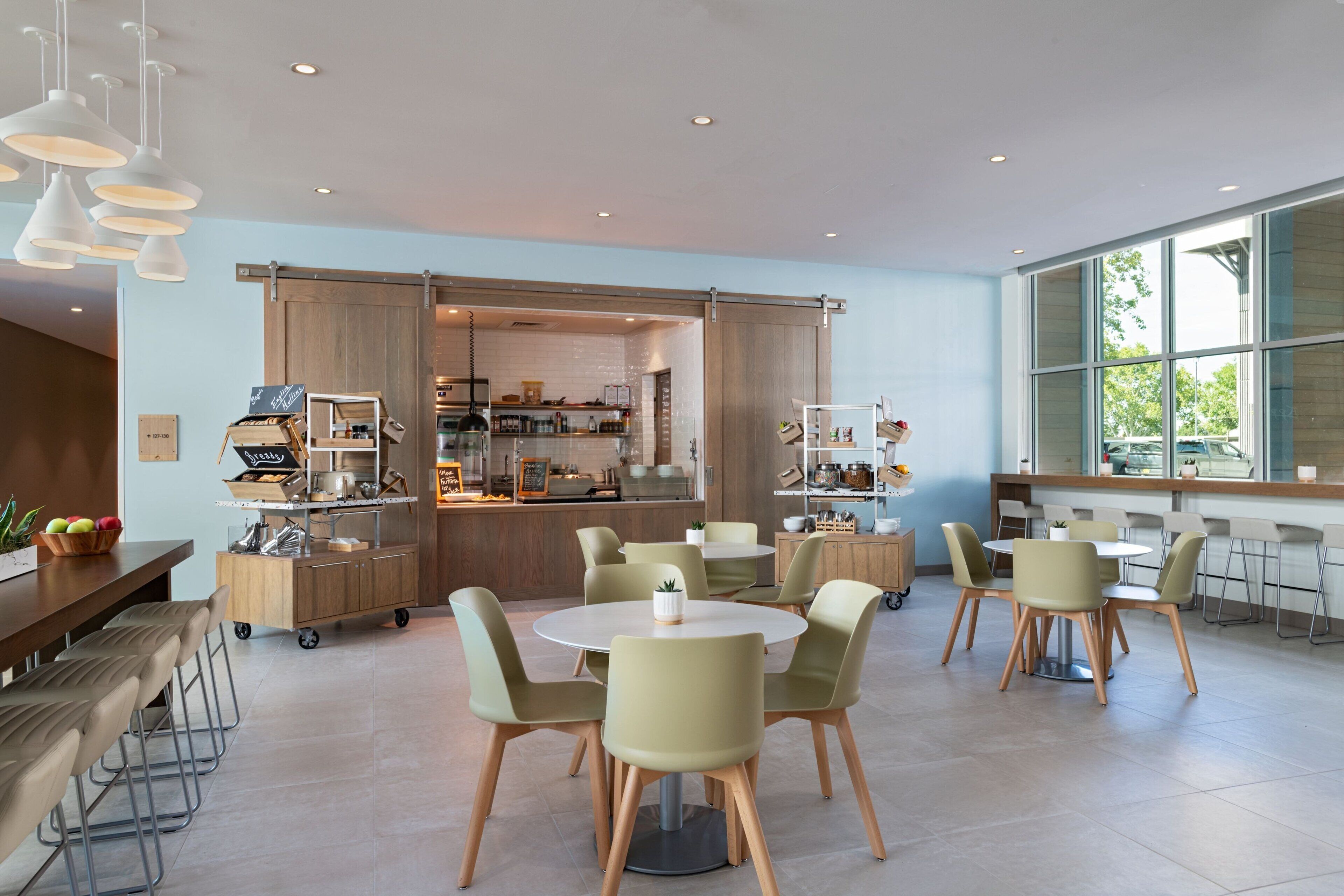 A modern cafe with round tables and chairs, a kitchen area, and large windows.